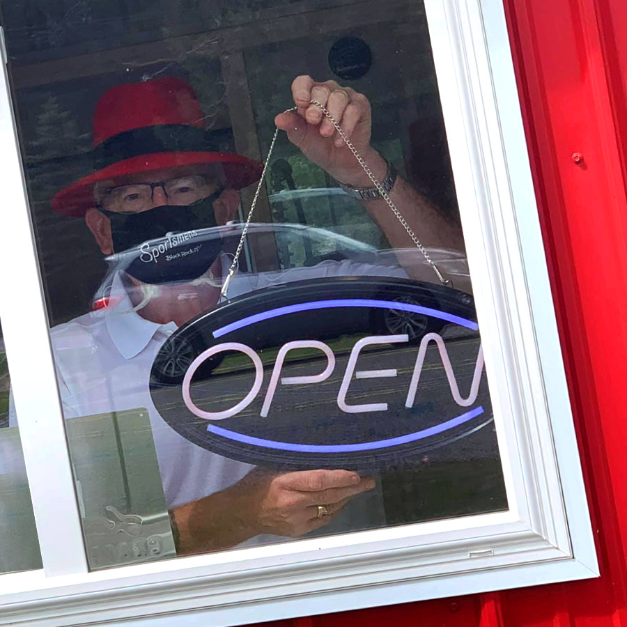 Master Distiller holding "OPEN" sign through tasting room window